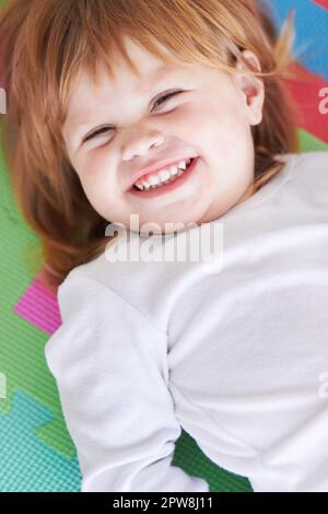 Jeune fille, rire et bonheur portrait d'un bébé sur un terrain de parc à la maison avec un sourire. Gingembre bébé, enfant rire et heureux dans une maison avec joie Banque D'Images