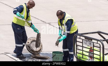 Deux hommes noirs africains travaillant à l'aéroport ou des employés dans des combinaisons et des gilets haute visibilité nettoient un réservoir de carburant à l'aéroport de Lanseria, Gauteng, en Afrique du Sud Banque D'Images