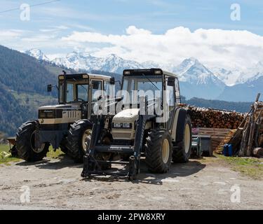 Deux tracteurs devant une pile de bois dans la ville alpine de Lignan au printemps. Aoste Vally, NW Italie. Montagnes enneigées derrière. Banque D'Images