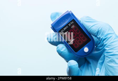 Oxymètre de pouls dans la main du médecin avec un gant sur fond bleu. Une main dans un gant médical tient un dispositif pour le diagnostic de santé Banque D'Images