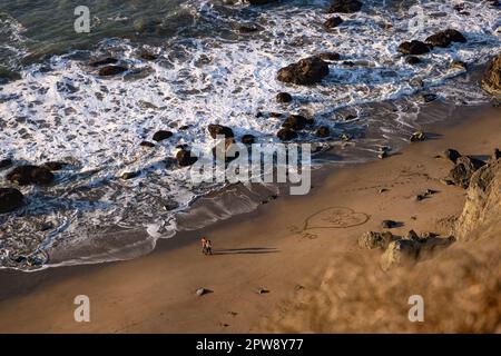 Une photo d'un couple marchant sur Baker Beach avec un coeur dessiné sur le sable. Banque D'Images