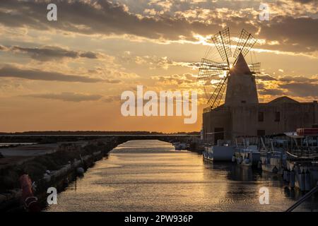 Moules à sel et moulins à vent pour le traitement du sel de mer. Entre eux. Ciel nuageux au printemps au coucher du soleil. Lagoon dello Stagnone, Marsala, Sicil Banque D'Images