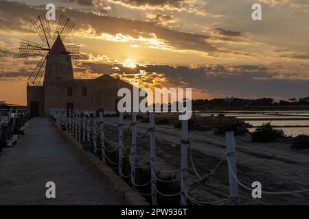 Moules à sel et moulins à vent pour le traitement du sel de mer. Entre eux. Ciel nuageux au printemps au coucher du soleil. Lagoon dello Stagnone, Marsala, Sicil Banque D'Images