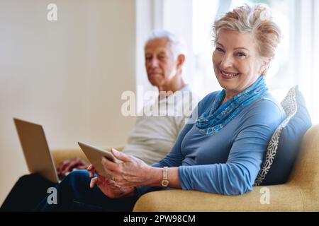 Les années de coucher du soleil sont les années les plus intelligentes. Portrait d'une femme âgée utilisant une tablette numérique alors que son mari utilise un ordinateur portable sur le canapé à la maison. Banque D'Images