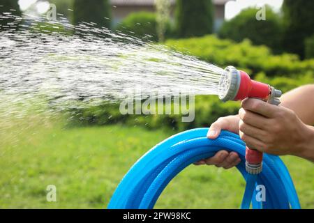 Homme pulvérisant de l'eau à partir d'un tuyau dans le jardin, gros plan Banque D'Images