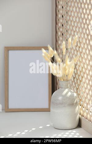 Cadre photo vierge et vase avec plante séchée sur seuil de fenêtre blanc Banque D'Images