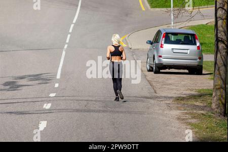 Fille dans un survêtement noir s'exerçant tout en courant dans un parc vert sur un tapis roulant Banque D'Images