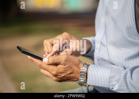 Détail des mains d'un homme Latino utilisant un téléphone portable. Banque D'Images