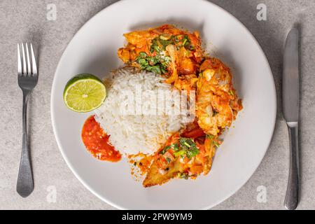 Délicieux Moqueca de poisson brésilien avec tomate, oignon, huile d'olive, coriandre et graines d'orocum. Servi sur une assiette en porcelaine blanche avec du riz. Vue de dessus. Banque D'Images