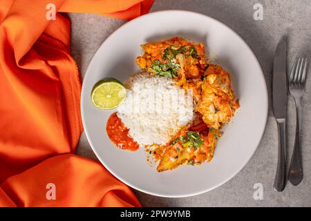 Délicieux Moqueca de poisson brésilien avec tomate, oignon, huile d'olive, coriandre et graines d'orocum. Servi sur une assiette en porcelaine blanche avec du riz. Avec orange à Banque D'Images