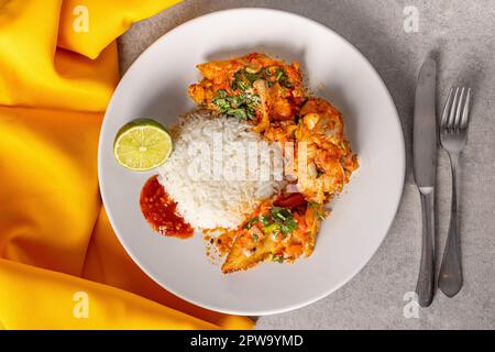 Délicieux Moqueca de poisson brésilien avec tomate, oignon, huile d'olive, coriandre et graines d'orocum. Servi sur une assiette en porcelaine blanche avec du riz. Avec jaune à Banque D'Images