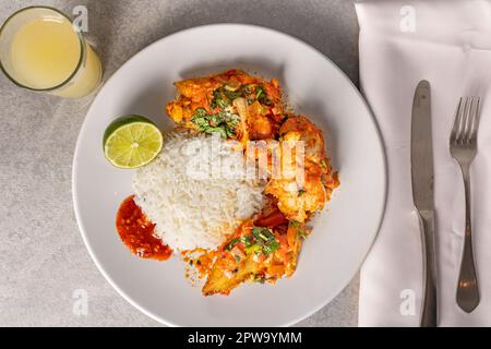 Délicieux Moqueca de poisson brésilien avec tomate, oignon, huile d'olive, coriandre et graines d'orocum. Servi sur une assiette en porcelaine blanche avec du riz. Avec noix de cajou ju Banque D'Images