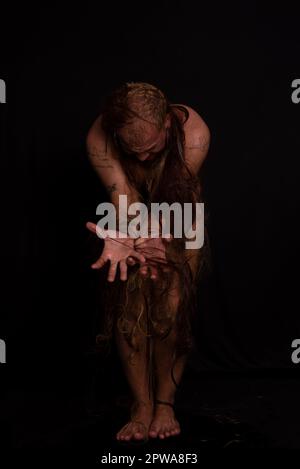 Jeune homme, acteur, portant bikini dans performance gorilla femme avec les cheveux partout dans son corps et expression de la douleur. isolé sur fond sombre. Banque D'Images