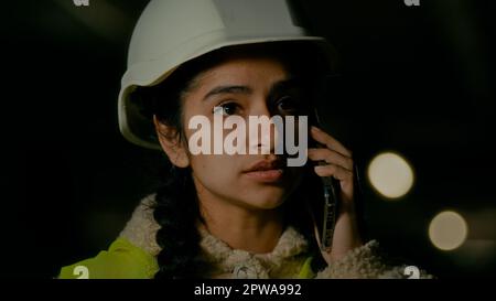 Jeune femme arabe professionnelle ingénieur technique architecte constructeur en uniforme et hardhat parlant téléphone mobile avec le travailleur de bâtiment discutant Banque D'Images