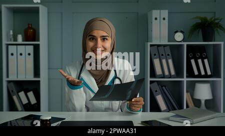 Médecin positif femme radiologue utiliser l'application de vidéoconférence parler avec le patient distant expliquer le résultat de la tomographie par IRM montrer l'image radiologique rendre virtuel Banque D'Images