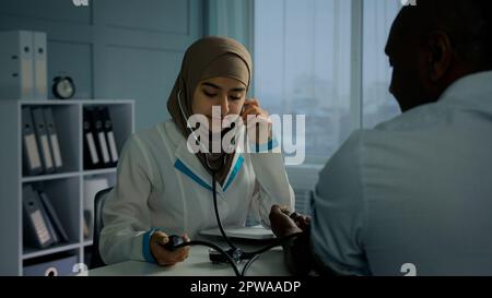 Médecin femme mesurant la pression artérielle avec un dispositif électronique utiliser un tonomètre médical femme cardiologue vérifier le rythme cardiaque de l'homme africain plus âgé Banque D'Images