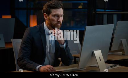 Un homme d'âge moyen du Caucase pensif s'assoit au bureau de nuit en pensant profondément à la pensée rêvant de nouvelles idées de projet d'affaires brainstorming résoudre le problème réfléchi Banque D'Images