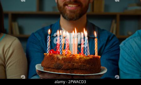 Gros plan gâteau de fête avec bougies en feu heureux barbu homme d'anniversaire méconnaissable sourire faire des fêtes avec des amis à la maison Banque D'Images