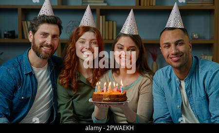 Les amis en chapeaux de fête célèbrent l'événement festif à la maison divers personnes multiraciales hommes femmes tiennent le gâteau d'anniversaire avec des bougies. Portrait de groupe souriant Banque D'Images