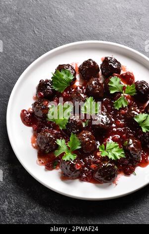 Boulettes de viande avec sauce aux canneberges sur une assiette blanche sur fond de pierre sombre. Vue rapprochée Banque D'Images