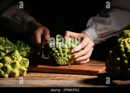 Femme coupant le brocoli Romanesco frais sur fond sombre, gros plan Banque D'Images