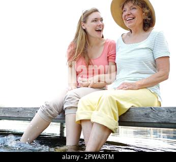 Amour et rire au lac - mère fille. Une mère et une fille rient ensemble tout en étant assis sur une jetée au bord du lac. Banque D'Images