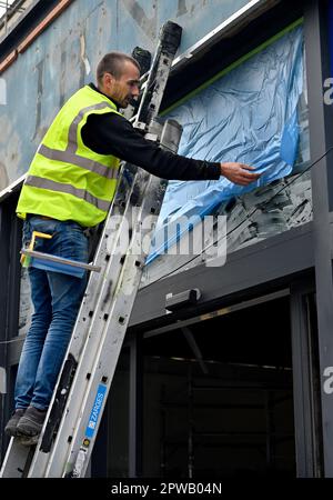 Workman sur l'échelle installer une feuille de masquage de protection en plastique sur la fenêtre en verre de l'atelier en vue de la peinture par pulvérisation Banque D'Images