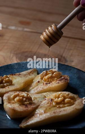 On peut apercevoir des doigts tenant une cuillère en bois spéciale en versant un filet de miel doré sur des poires cuites. Banque D'Images