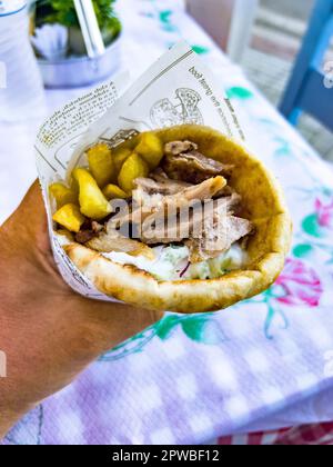 Main humaine tenant un gyros à la viande grecque enveloppé de pain pita et servi avec des pommes de terre frites et de la sauce tzatziki. Destination de voyage et alimentation Banque D'Images