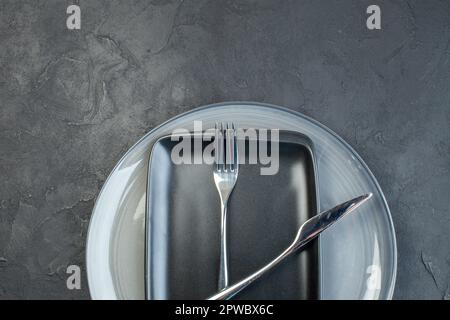 vue de dessus assiette noire avec couteau à fourche et assiette grise sur fond sombre argenterie salle à manger coloré féminité couverts faim dames grâce Banque D'Images