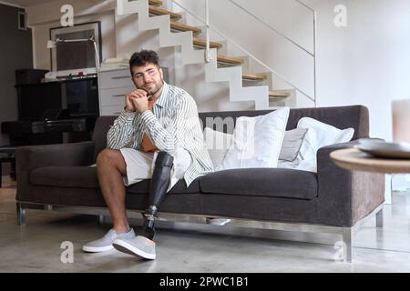 Jeune homme d'amputation réfléchi avec prothèse de jambe assis sur un canapé. Banque D'Images