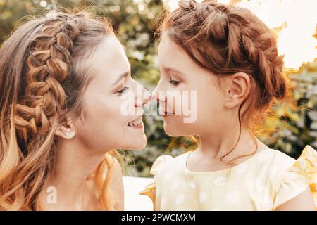 Maternité et maternité aimante. Belle jeune maman avec des cheveux tressés embrassant sa jolie petite fille douce tout en passant du temps ensemble à l'extérieur Banque D'Images