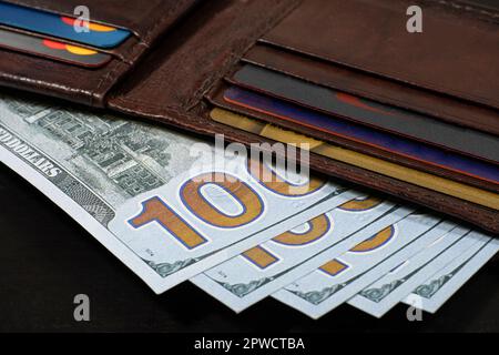 Portefeuille en cuir marron rempli de 100 USD de billets sur table noire. Banque D'Images