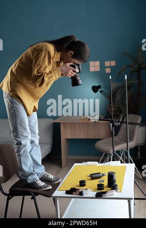 Photographe féminine prenant des produits de beauté sur la table en étant debout sur la chaise. Photographie professionnelle. Femme prend des photos de maquillage et de soin de la peau Banque D'Images