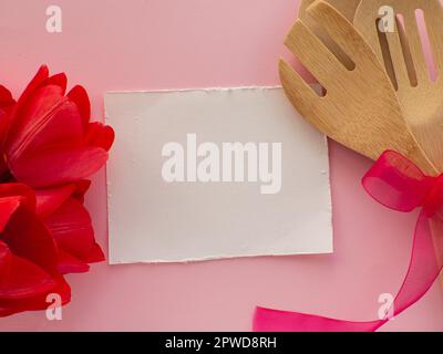 Tulipes rouges fleurs avec outils de cuisine sur fond rose avec papier blanc avec espace de copie. Carte de voeux pour la fête des femmes et des mères. Anniversaire félicitations Banque D'Images