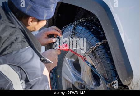 Homme mettant des chaînes à neige sur les roues de sa voiture pour améliorer la traction en hiver. Banque D'Images