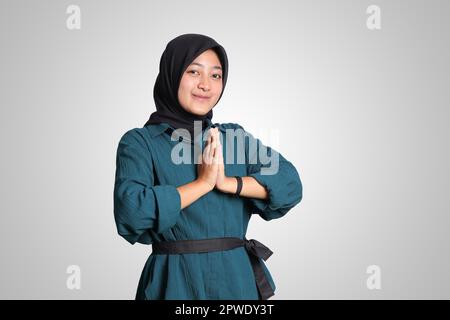 Portrait de la gaie asiatique hijab dans une chemise décontractée, montrant des excuses et le geste de la main de bienvenue. Concept publicitaire. Image isolée sur fond blanc Banque D'Images