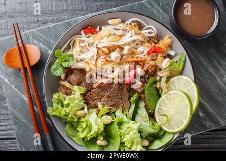 Pho Bo Tron salade de nouilles de boeuf mélangé est un plat populaire dans la cuisine vietnamienne à proximité sur le bol sur une table en bois. Vue horizontale du dessus Banque D'Images