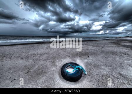 Alter Reifen am Strand mit Netzresten, vieux pneu sur la plage avec des morceaux de filet Banque D'Images