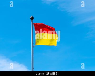 Un drapeau rouge et jaune permettant de nager sur la plage. Un drapeau sur fond bleu ciel. Banque D'Images