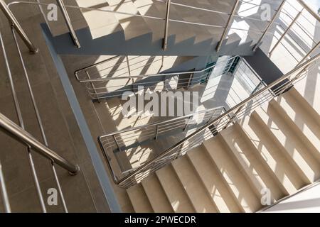 Escaliers dans un immeuble de bureaux en béton dans des tons neutres, recouverts de carreaux de céramique, avec des rails en métal brillant en acier inoxydable, glaçure importante Banque D'Images