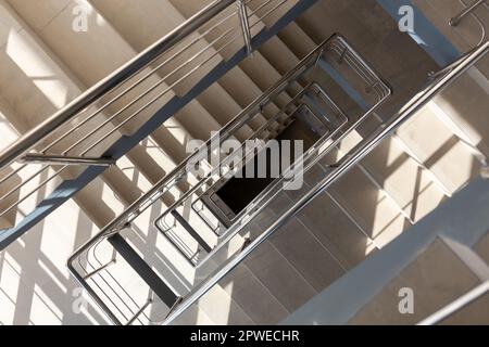 Escaliers dans un immeuble de bureaux en béton dans des tons neutres, recouverts de carreaux de céramique, avec des rails en métal brillant en acier inoxydable, glaçure importante Banque D'Images