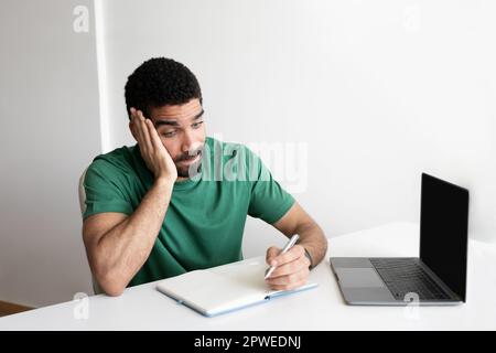 Triste fatigué jeune arabe homme blogueur à la table avec ordinateur portable avec écran vide de travail, a appel vidéo Banque D'Images