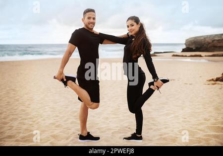 Heureux couple sportif qui s'étire pour les jambes, s'échauffe avant de s'entraîner sur la plage de l'océan, regardant et souriant à la caméra Banque D'Images