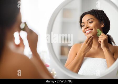 Concept de soin de la peau. Belle femme noire massant visage avec outil gua sha Banque D'Images