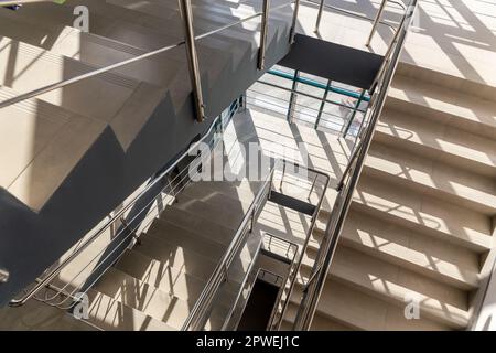 Escaliers dans un immeuble de bureaux en béton dans des tons neutres, recouverts de carreaux de céramique, avec des rails en métal brillant en acier inoxydable, glaçure importante Banque D'Images