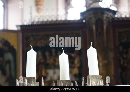 Trois bougies blanches placées dans un lustre dans une église. Sur le fond il y a l'autel défoqué. Banque D'Images