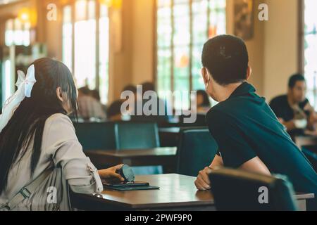 Vue arrière de la femme asiatique avec sac à dos tenant la file d'attente sans fil de la machine à appelants à la main pour attendre la nourriture dans le restaurant. Le pager d'avertissement de signal d'alarme se trouve en mode autonome Banque D'Images