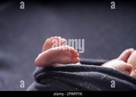 Bébé de petite taille pieds nus croisés sur une couverture bleu marine. vue rapprochée du pied de bébé le bébé est enveloppé confortablement dans une couverture bleue. nouveau-b Banque D'Images