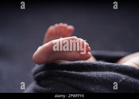 Bébé de petite taille pieds nus croisés sur une couverture bleu marine. vue rapprochée du pied de bébé le bébé est enveloppé confortablement dans une couverture bleue. nouveau-b Banque D'Images